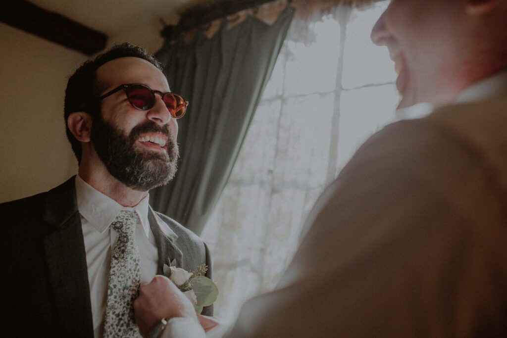 groom smiling as groomsmen helps to put on his boutoniere