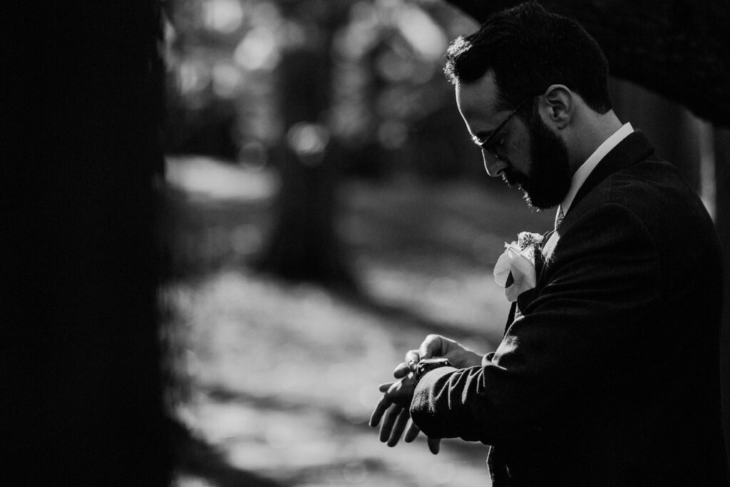 black and white photo of groom looking at his watch as he waits for the first look