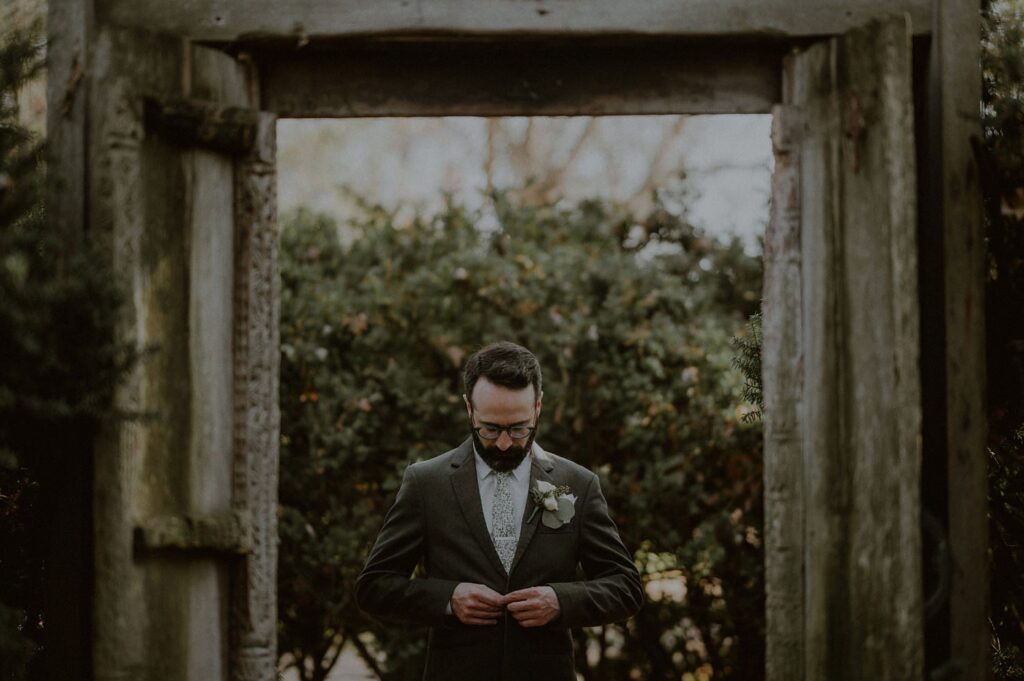 groom buttoning up his suit, as seen through the frame of the doorway