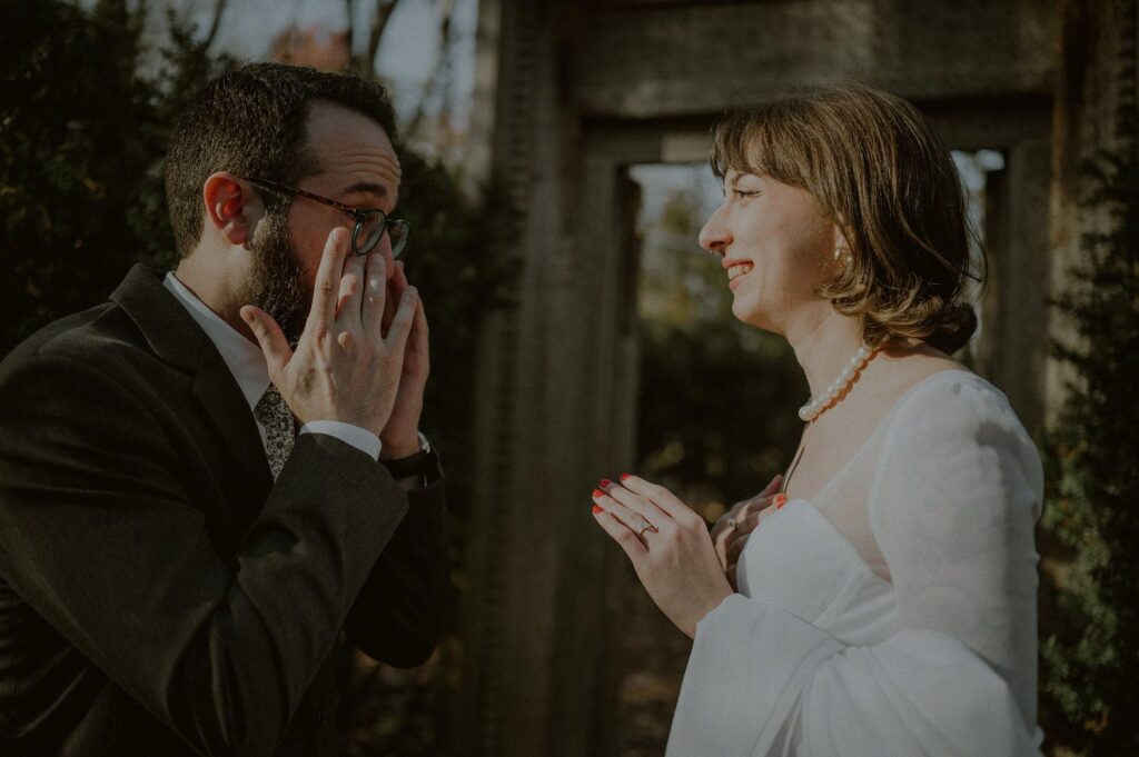 groom wiping off tears as bride laughs and smiles after their first look