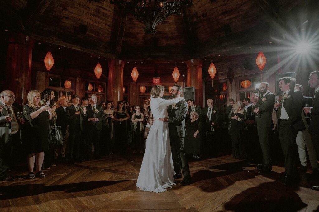 bride and groom first dance in front of wedding guests in dimly lit room