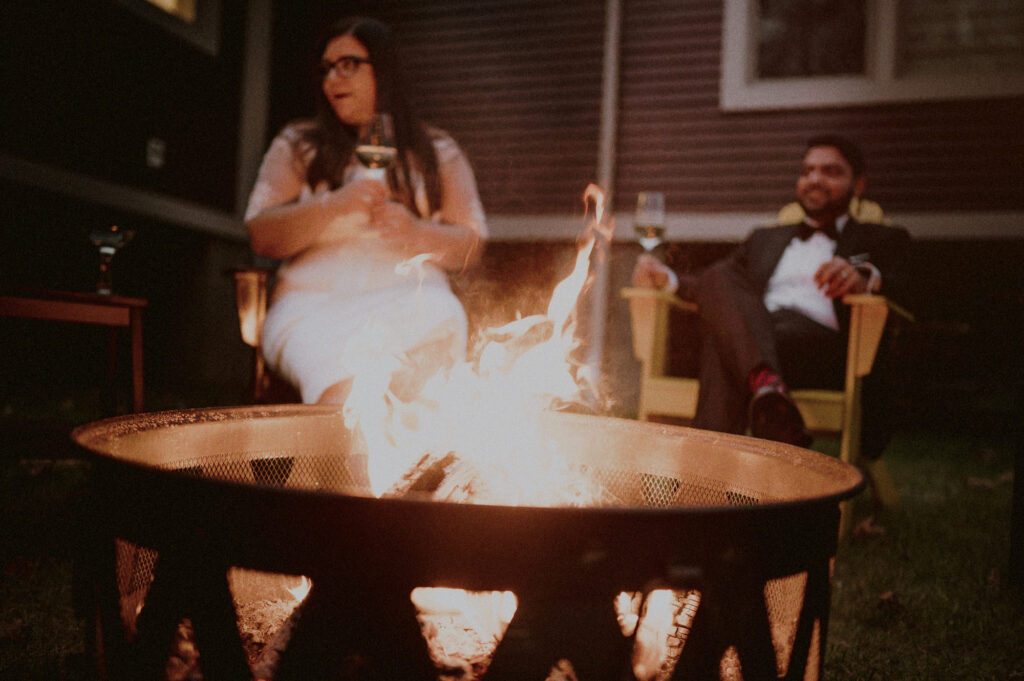 couple sitting in front of fire pit in backyard casually celebrating after elopement in their home