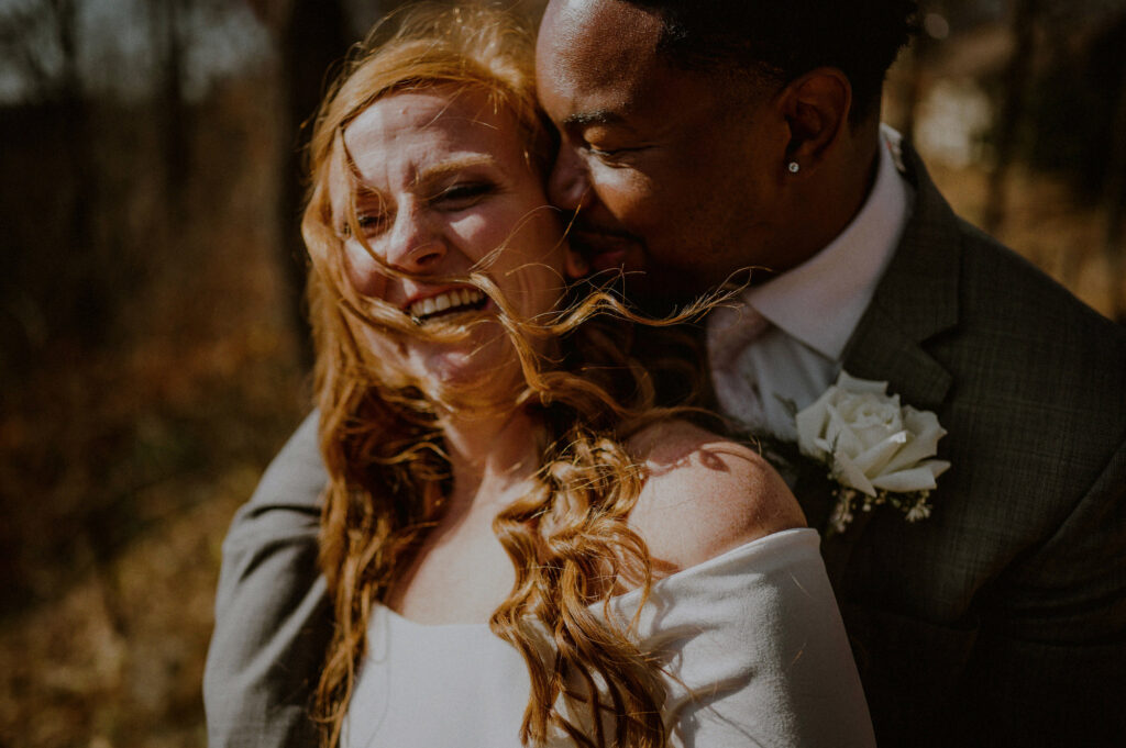 portrait of couple embracing and laughing as wind blows woman's hair