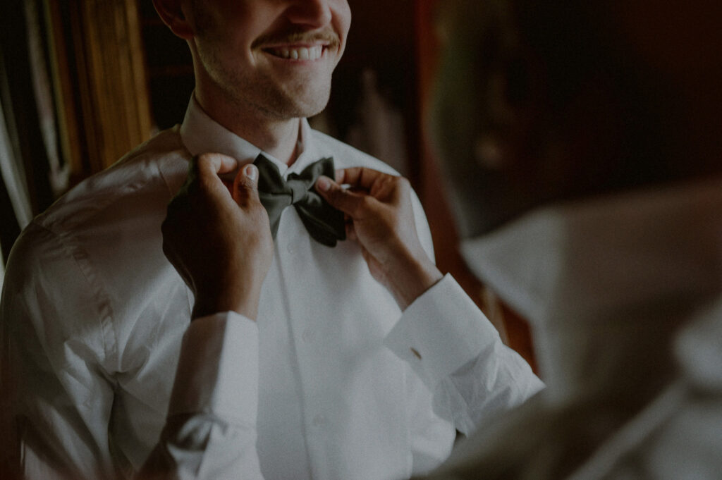 same sex couple gets ready together for wedding as they adjust each other's ties