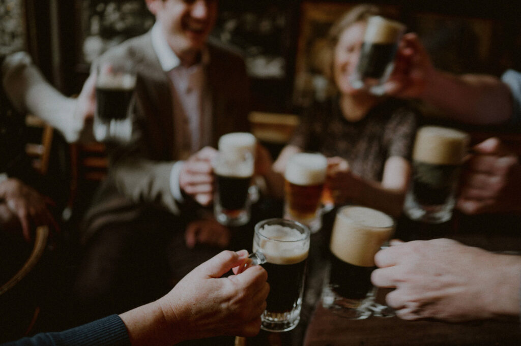 clinking glasses of beer with out of focus faces in background in celebration of elopement