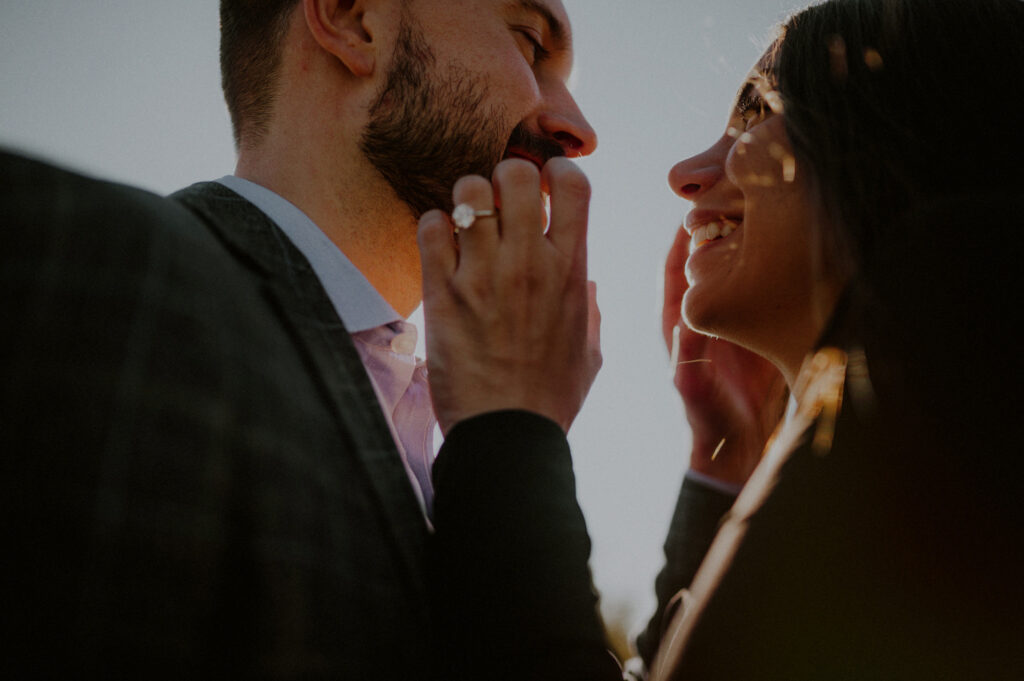 woman and man looking at each other against sunlight, and woman holding up hand with engagement ring