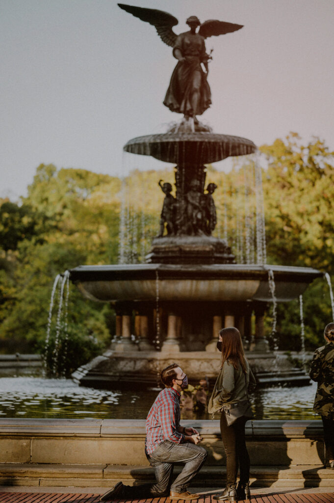 man on one knee proposing to girl in front of bethesda fountain in nyc