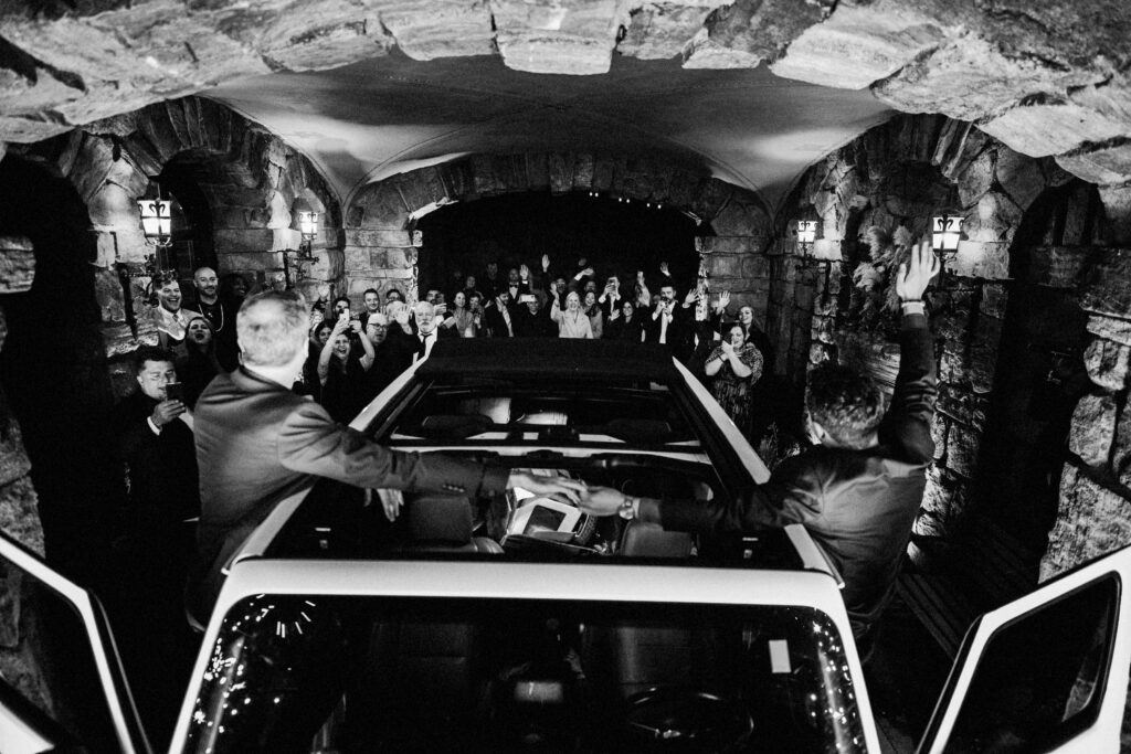 two grooms grand exit from wedding reception  from point of view of front of car looking at audience